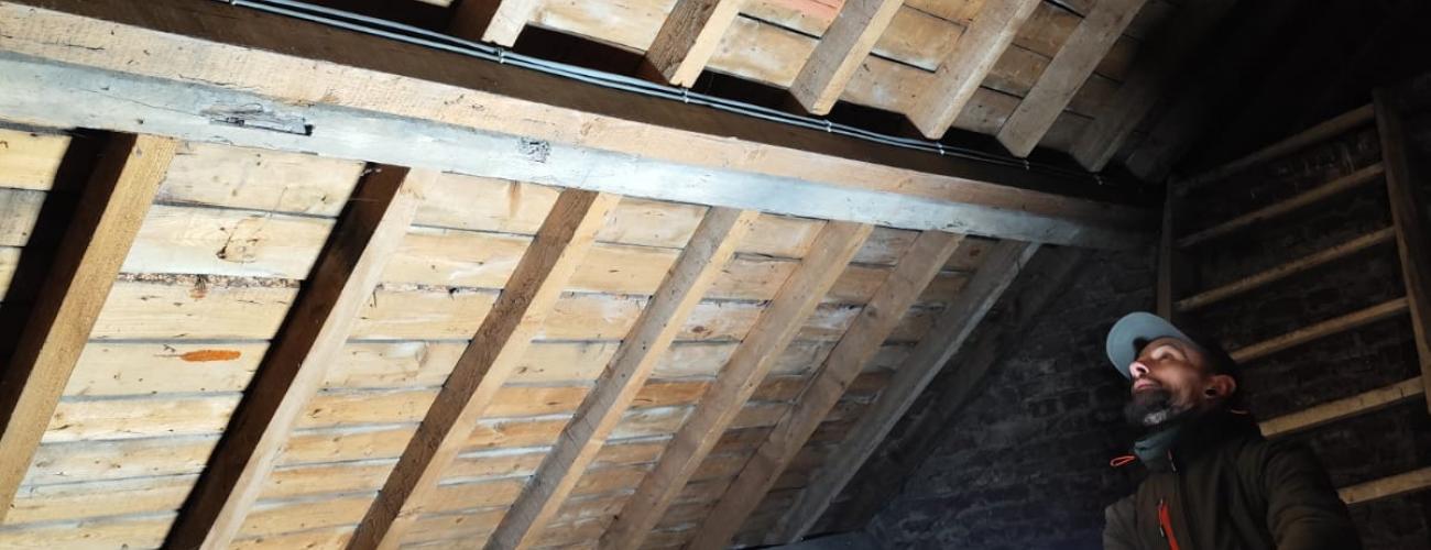 Un homme examine l'intérieur d'un grenier en bois, éclairé par une lampe, sous une toiture